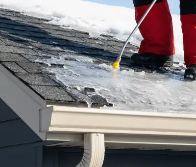 Ice dam removal technician using a steam wand to melt thick ice buildup on a residential roof in Madison, WI
